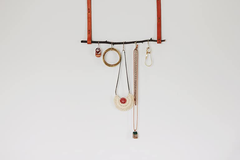 a tree branch hanging from leather straps with hooks to hold necklaces