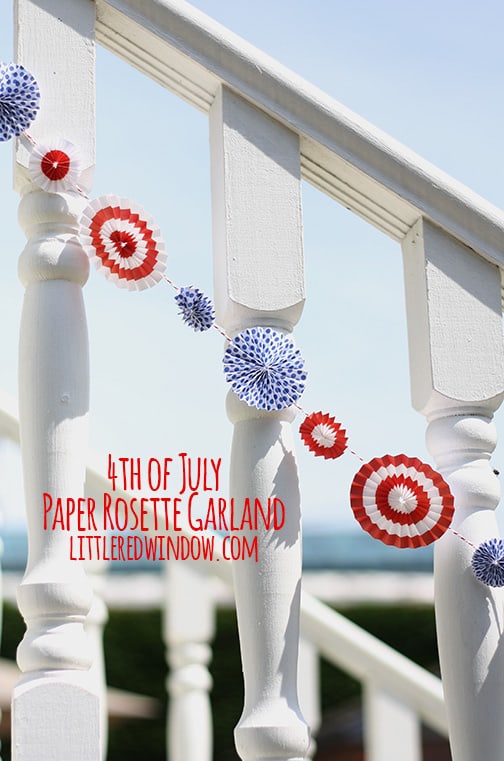 Red and white rosettes strung on baker's twine and hanging along a white railing outside