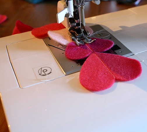 Closeup of sewing machine sewing pink felt hearts in a line down their centers