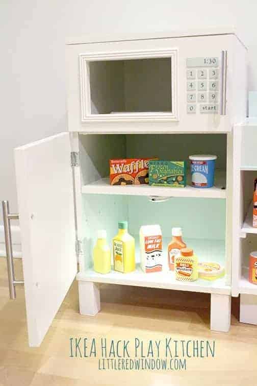 Closeup of the fridge/microwave with the fridge door open, interior light on, and play food inside