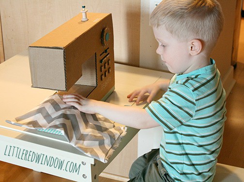 little boy sitting at a table and playint with a scrap of fabric and play sewing machine