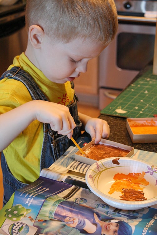 little boy in overalls painted a gift box with a paintbrush