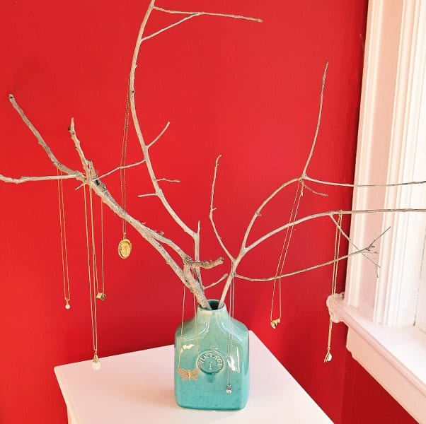 blue ceramic vase with tree branches sticking out and necklaces hanging from them
