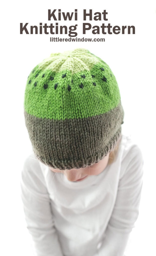 small child modeling brown and green knit kiwi hat knitting pattern with black seeds