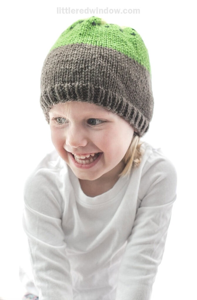 laughing girl wearing a white shirt and brown and green knit kiwi hat