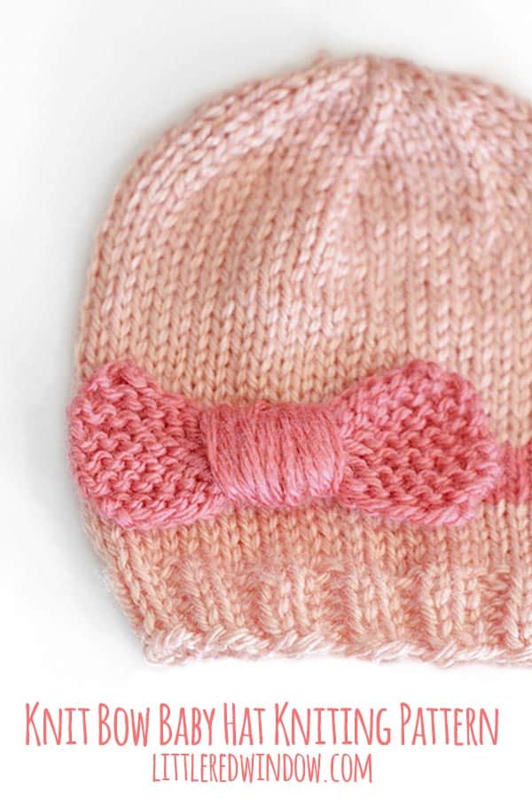 closeup of a light pink knit hat with a hot pink bow around the middle laying flat on a white background