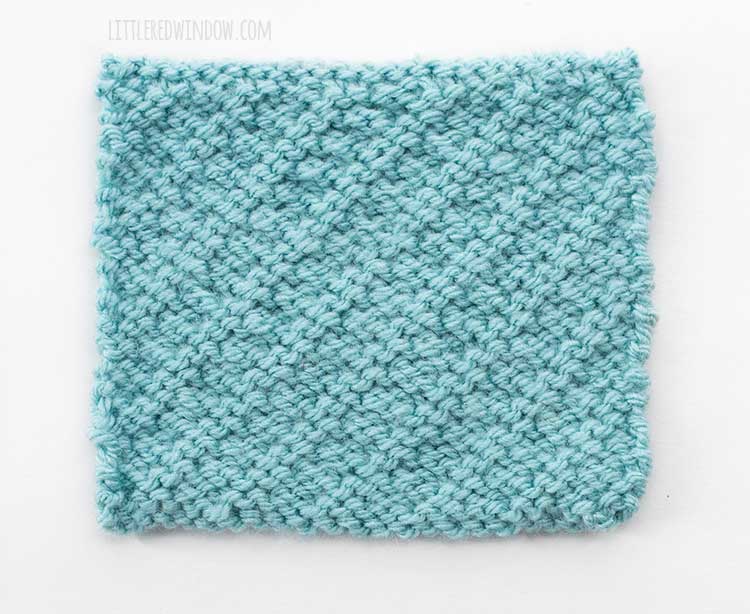 The wrong side of a square of light blue swatch of diagonal woven slip stitch knitting on a white background