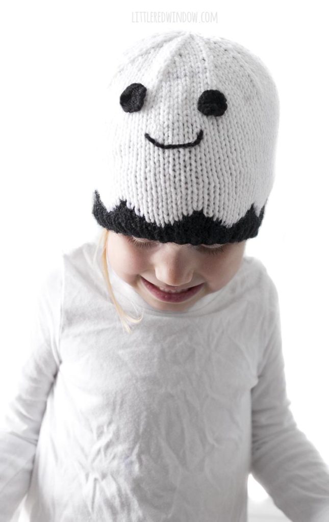 Little girl wearing smiling white ghost knit hat and looking down