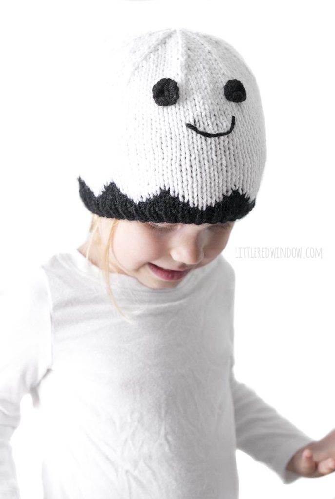 Little girl wearing smiling white ghost knit hat and looking down and to the right