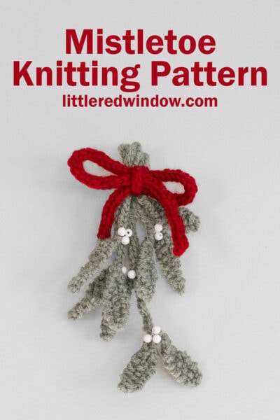 Knitted mistletoe with green leaves, white berries, and a red bow on a light background. Text above reads: