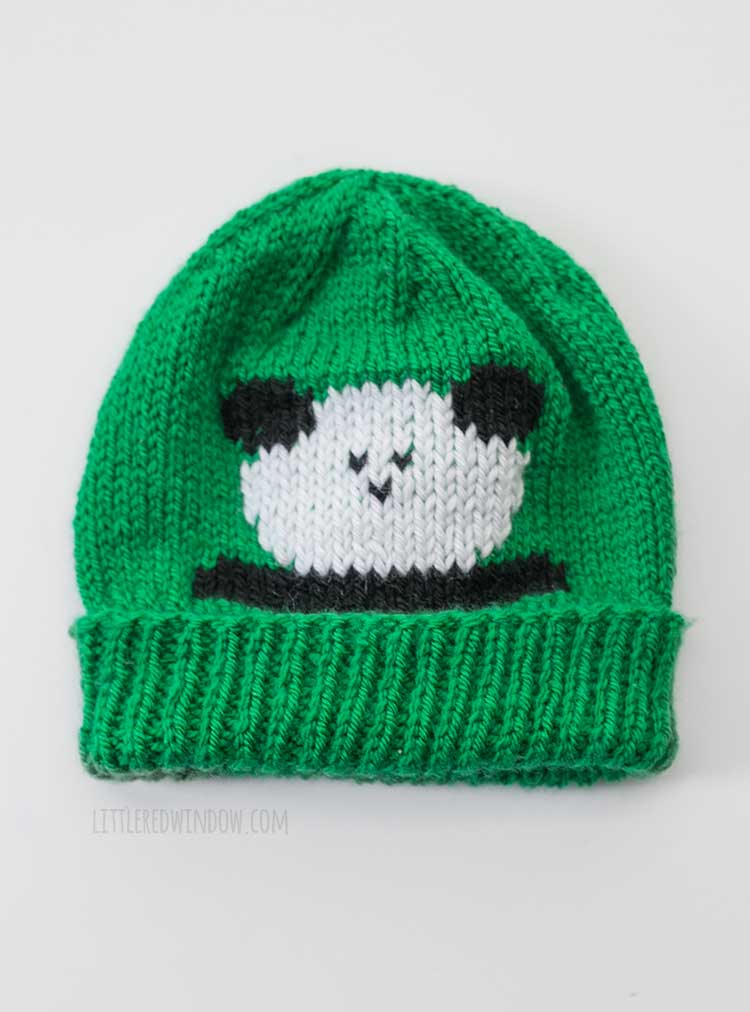Flat lay of kelly green knit has with a panda on the front in front of a white background