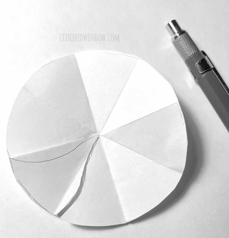 white circle that has been folded into eighths with one peppermint candy section sketched next to a mechanical pencil on a white background