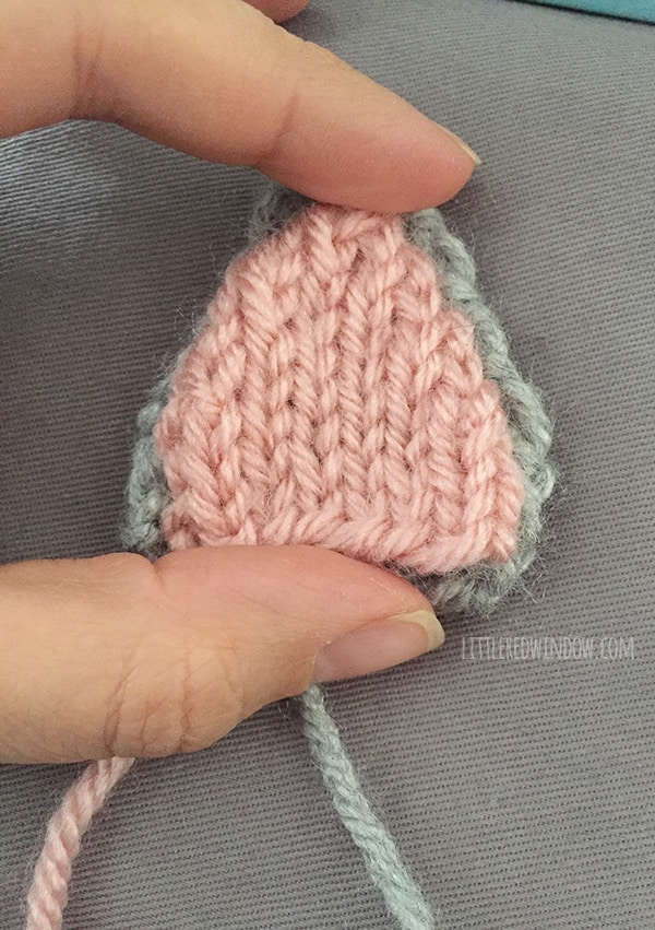 Hand holding the assembled knit cat ear that is gray on the outside and pink on the outside