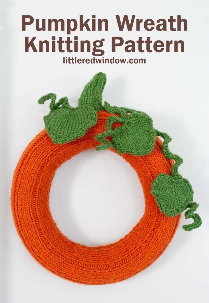 A knitted pumpkin wreath adorned with green leaves and vines, resembling a festive pumpkin. The text
