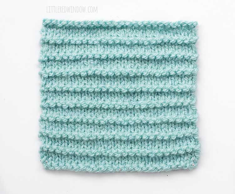 The right side of a light blue square swatch of stockinette stitch knitting with evenly spaced purl ridges across horizontally
