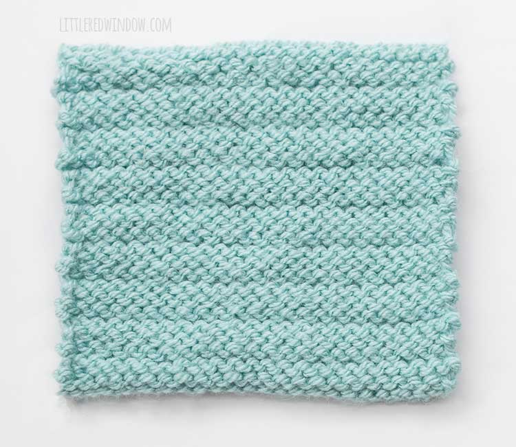 The wrong side of a light blue square swatch of stockinette stitch knitting with evenly spaced purl ridges across horizontally
