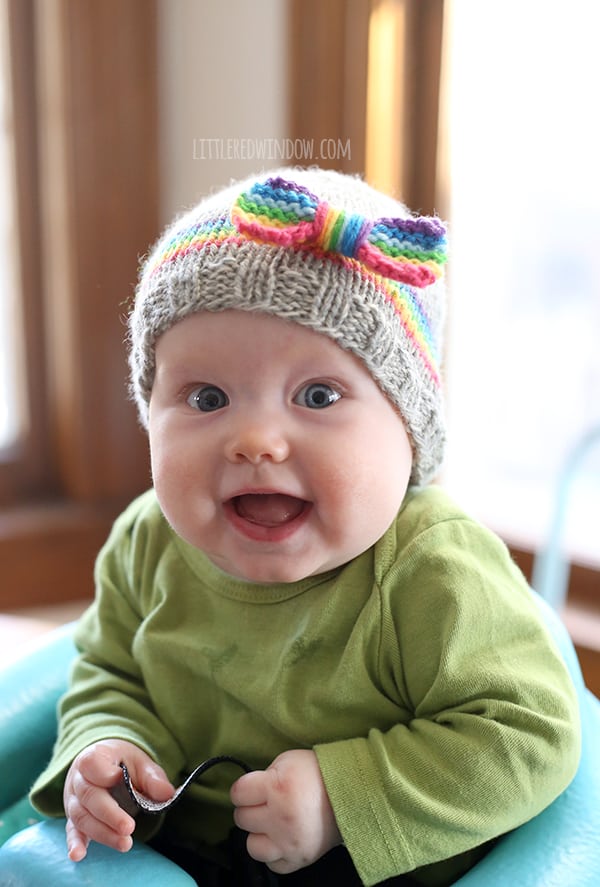 Laughing baby in green shirt wearing rainbow bow hat