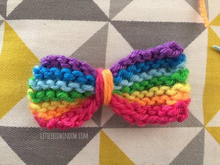 rainbow striped knit bow with a piece or pink and orange string wound around just left of center
