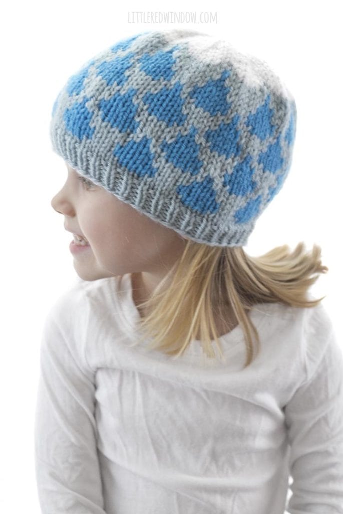 little girl wearing light blue knit hat with blue raindrop pattern and white cloud on top look off to the left