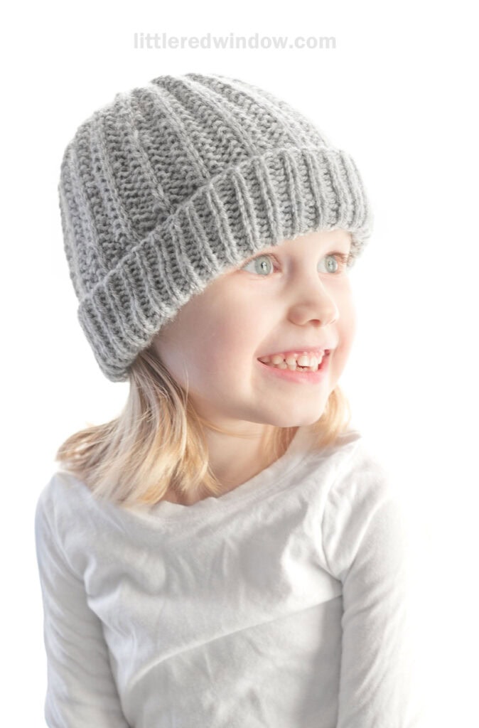 smiling girl in gray ribbed knit hat looking off to the right with light on her face