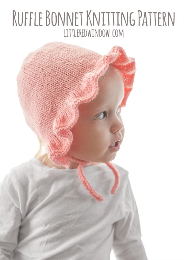 side view of chubby toddler in white shirt in front of a white background wearing a light pink ruffle bonnet knitting pattern with chin ties and looking off to the right