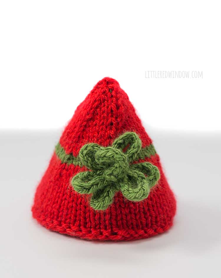 a small red knit Christmas present cone tree with a green knit bow on the front