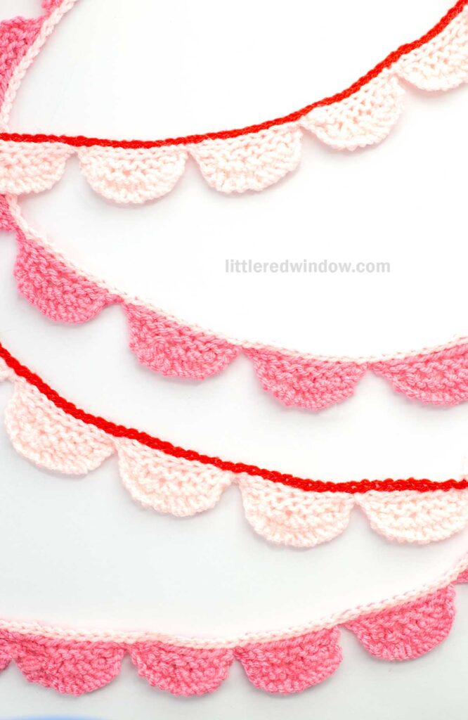 Crocheted heart-shaped bunting in shades of red, pink, and white arranged in rows on a white background.