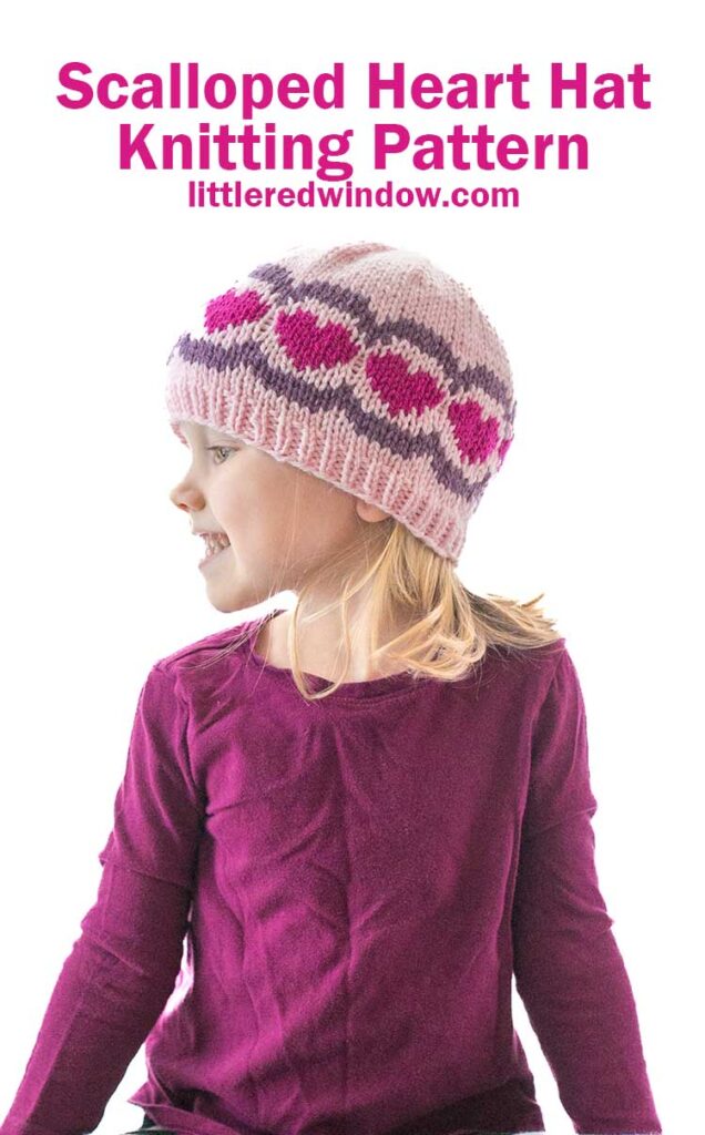The child, donning a scalloped heart hat in hues of pink and purple, gazes thoughtfully to the side. Her ensemble is completed with a long-sleeve purple shirt. The text above reads,
