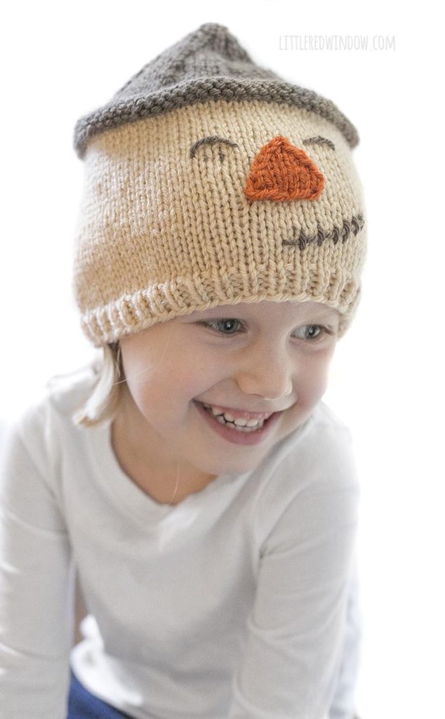 little girl smiling and wearing smiling scarecrow hat