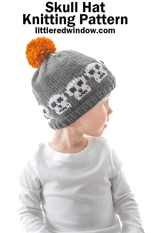 Child wearing a gray knitted hat with white skull designs and an orange pom-pom on top. They are dressed in a white long-sleeve shirt and looking to the side. Text above reads,
