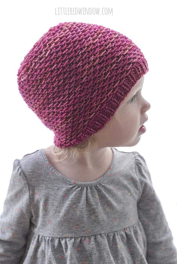 Little girl wearing magenta knit hat knit in slipped purl stitch and looking off to the right