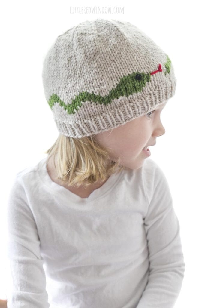 side view of girl wearing snake hat knitting pattern in tan with a green snake around the middle