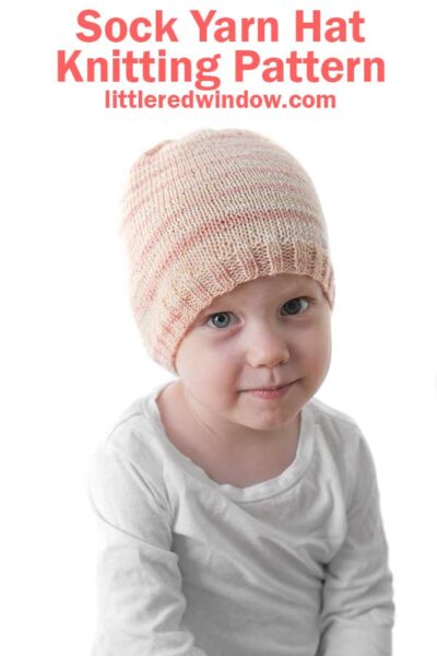 smirking baby looking at the camera and wearing a light pink sock weight yarn knit hat