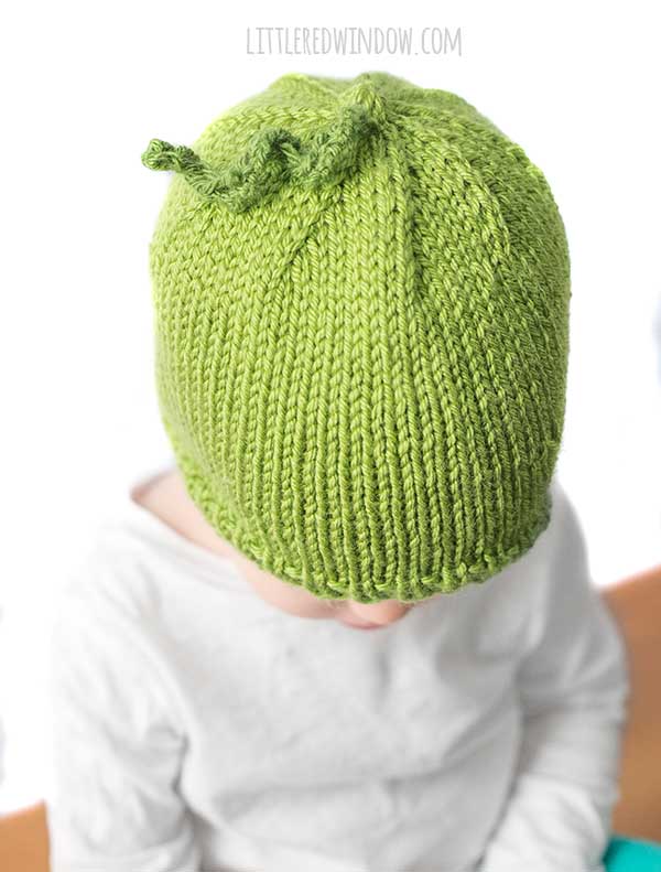 view from above of baby wearing sweet pea hat in bright green with a slightly darker green curly knit tendril on top to look like a peashoot
