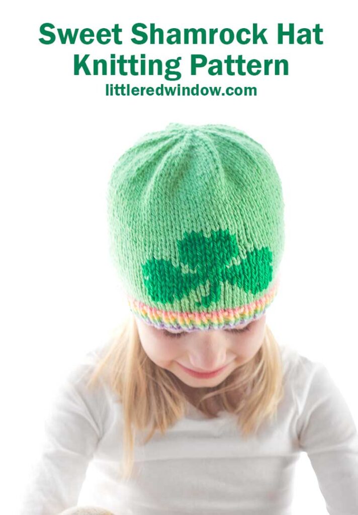 Child sporting a cozy green hat adorned with a shamrock design and a vibrant rainbow brim. Text above reads: