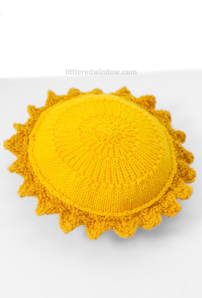 bright yellow knit sun with mustard yellow sun rays around the outside on a white background from above