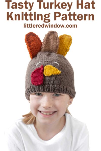 Child wearing a knitted turkey hat with colorful knitted feathers on top. The text reads "Tasty Turkey Hat Knitting Pattern" and "littleredwindow.com." The child is smiling and wearing a white shirt.