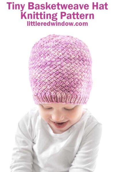 A smiling baby wears a pink, hand-knitted Tiny Basketweave Hat and a white shirt, with text above reading "Tiny Basketweave Hat Knitting Pattern littleredwindow.com".