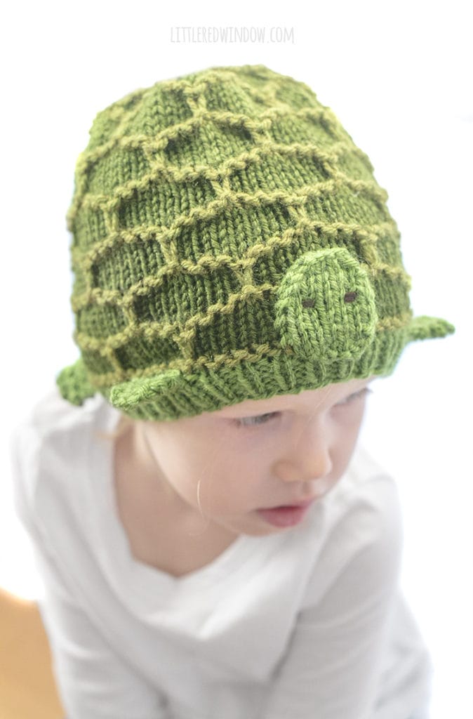 little girl wearing green turtle hat looking down an to the right