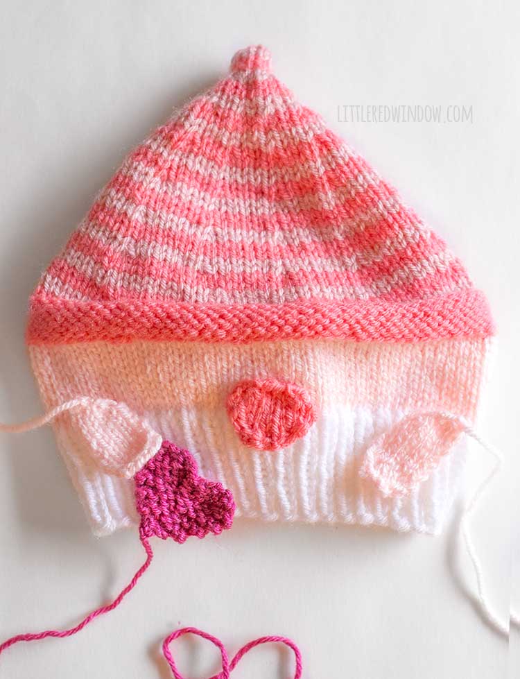 flat lay image showing the knit valentine gnome hat with the gnome arms and heart placed on top to show were to sew them to the hat