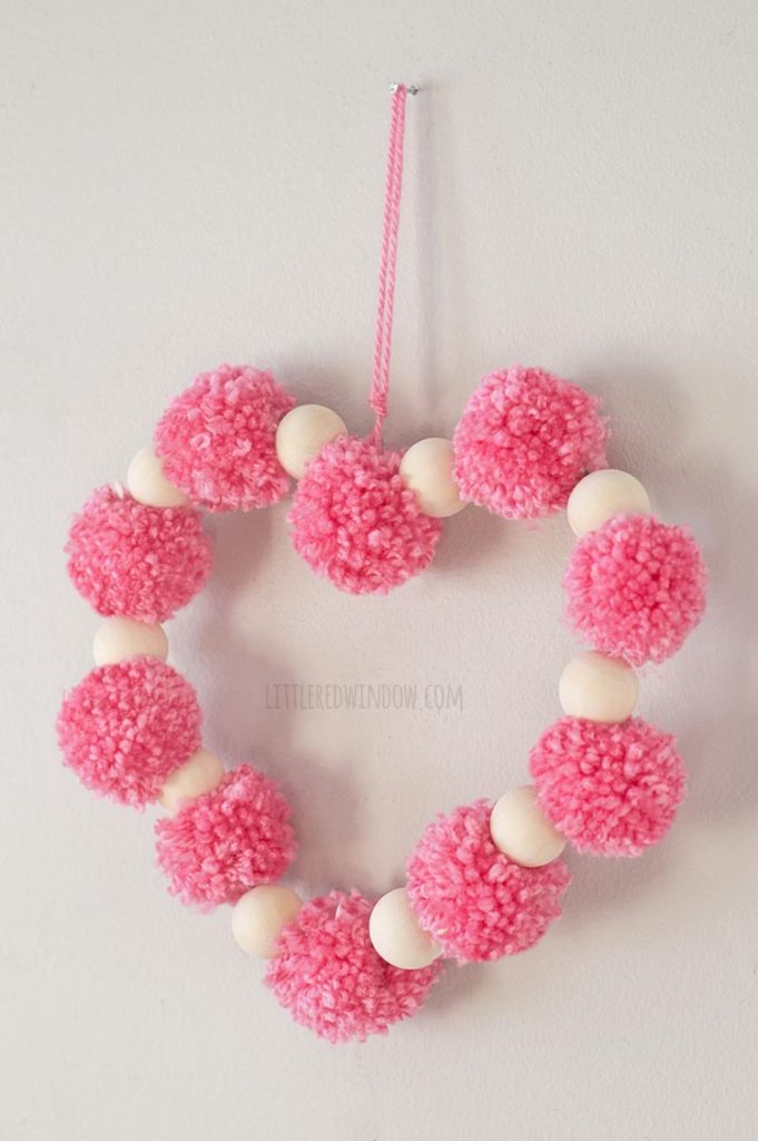 right angle view of heart shape made of pink pom poms and wood beads