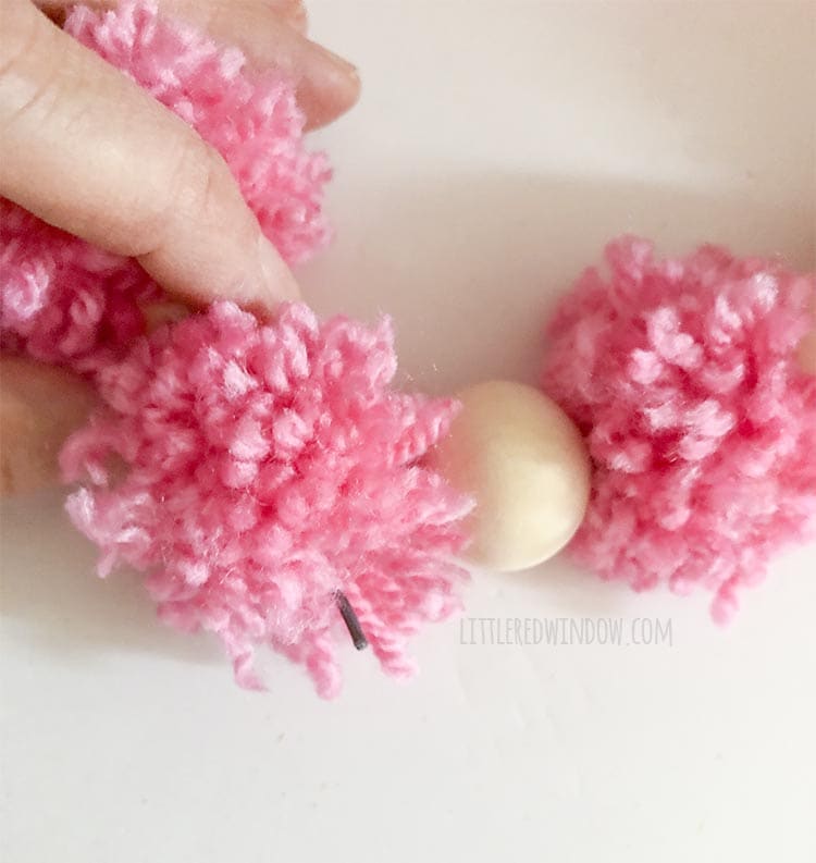 hand holding the other wire end showing that end of the wire poking through a pom pom