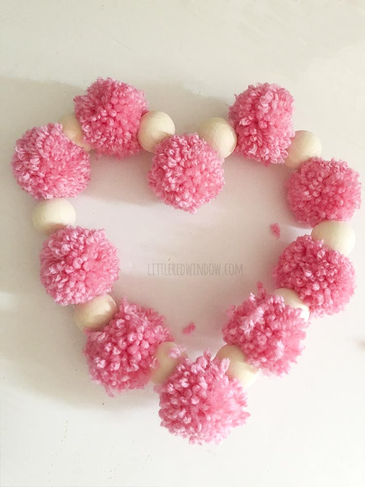 overhead view of finished valentine pom pom heart craft on a white background