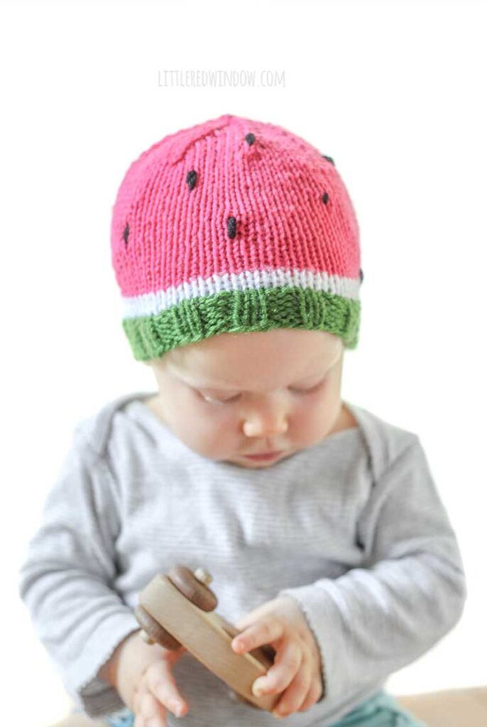 baby wearing a fun knit hat that looks like a watermelon slice complete with seeds looking down at their hands