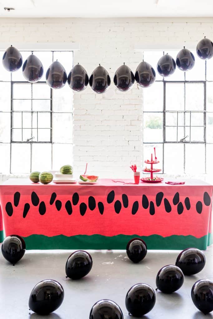 Party room with a long table covered in a watermelon print table cloth and black seed balloons everywhere