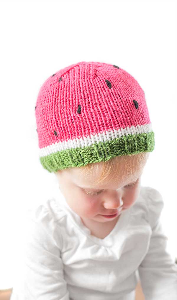 baby wearing a fun knit hat that looks like a watermelon slice complete with seeds looking down to the right