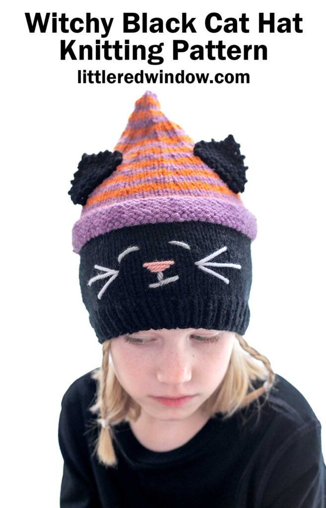 A person is wearing a knitted hat that looks like a black cat with a striped purple and orange top section. The hat features black cat ears, white whiskers, a pink nose, and white eyes. The text above the image reads 