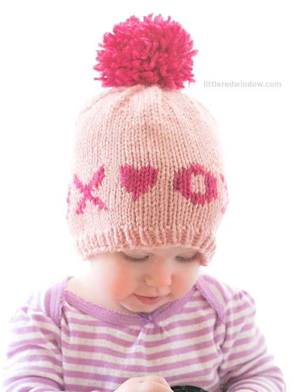 A baby wearing a charming valentine hat featuring a pink pom-pom and