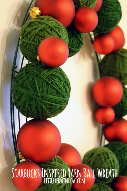 side view of Wreath made of green yarn balls and red Christmas ornaments hanging on a wall