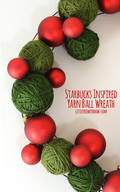 closeup of Wreath made of green yarn balls and red Christmas ornaments hanging on a wall